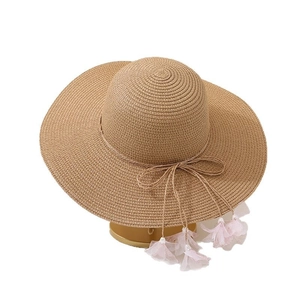 Wide brim straw sun hat with decorative ribbon and pink floral tassel on white stand