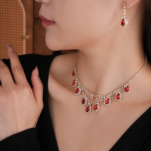 Detailed view of model wearing gold jewelry set with red teardrop stones and tassels