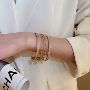 Detail of multi-layer gold cuff bracelet with cubic zirconia worn on model in white suit