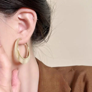 Detail of cream acrylic C-hoop earring with gold trim worn by a model in soft light