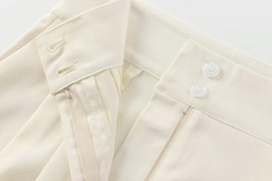 Détail du pantalon de costume beige montrant la double fermeture à bouton et le tissu
