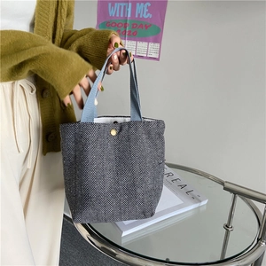 Close-up of a minimalist herringbone tweed handheld lunch bag featuring a gold button closure