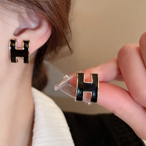 Macro shot of H-shaped black enamel stud earrings with gold plating finish details