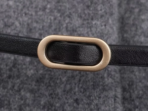 Dettaglio di una cintura nera sottile con fibbia ovale dorata su un cappotto di lana