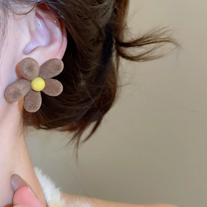 Close-up of brown flocked flower stud earring with yellow center worn on ear