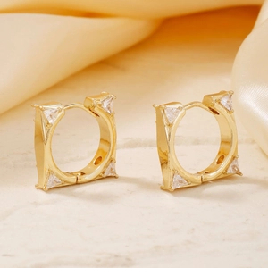Elegante goldene quadratische Creolen mit dreieckigen Zirkonia auf beigem Steinhintergrund