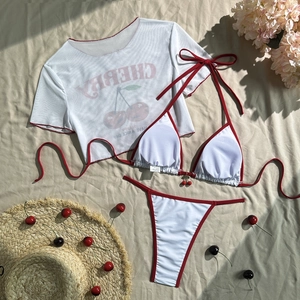 Detailed flat lay of white three-piece bikini with cherry print and mesh cover-up top