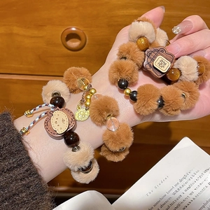 Détail d'un bracelet en perles de bois et pompons avec breloque dorée sur fond chaleureux