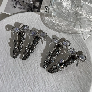 Close-up of four silver bow hair clips with dark grey crystals on a white textured plate