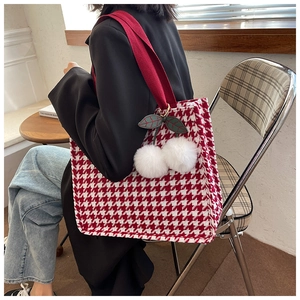 Detail of red houndstooth tote bag with plush cherry charm worn by model in a cafe
