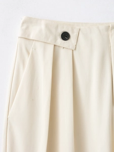 Détail du pantalon en sergé beige montrant le bouton, la taille plissée et la poche