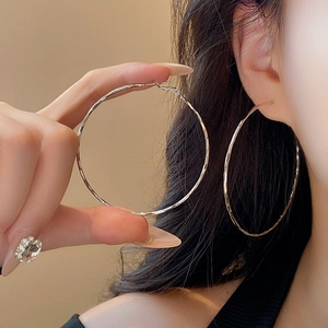 Macro shot of large silver hoop earrings with a textured hammered finish on a model