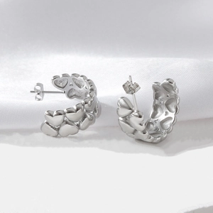 Detailed close-up of silver C-shape earrings with embossed heart pattern on white fabric