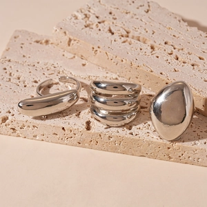 Macro shot of polished silver geometric rings displayed on natural travertine stone base