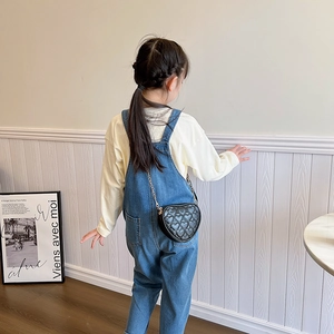 Girl wearing denim overalls and black quilted heart chain crossbody bag in casual setting