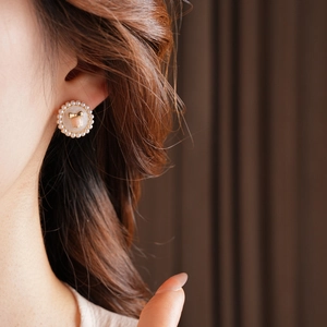 Detail of vintage round pearl earrings with golden bow on a model against dark curtains