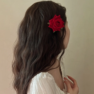 Detail of a romantic red rose hair clip with green leaf on long wavy brown hair