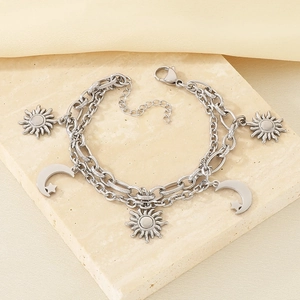 Detail view of silver double-layered bracelet with sun and moon pendants on stone background