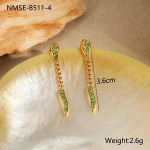 Detail view of gold drop earrings with green zircon stones on a shell background