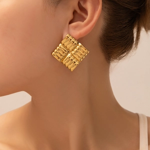 Close-up of geometric square pleated gold earrings with textured metal surface