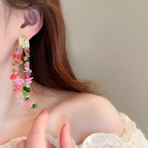 Close-up of long colorful crystal tassel earrings worn on a model with gold studs