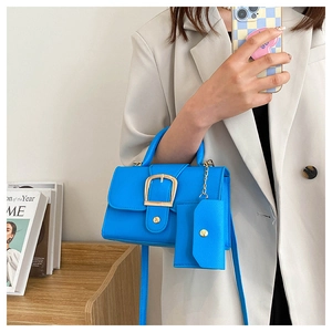 Detail of bright blue leather crossbody bag set with gold horseshoe buckle on light suit