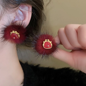 Elegant red plush ball stud earrings with gold trim worn by a model in soft light