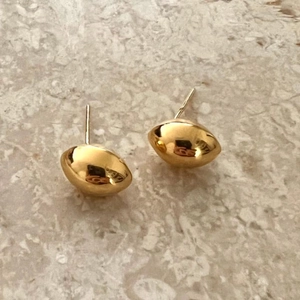 Close-up of polished gold bean-shaped S925 silver stud earrings on marble background