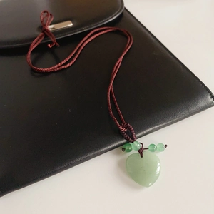 Detailed view of a green jade heart pendant on a red braided rope necklace over a bag