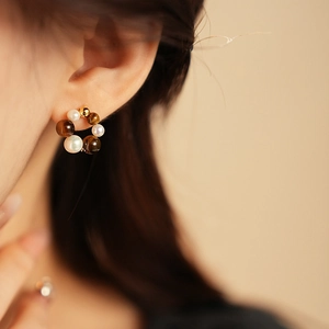 Detail of round pearl and gold bead stud earrings with brown gemstone on ear
