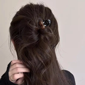 Detail of a black hair claw clip with brown beads holding a half-up hairstyle on model