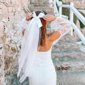 Detail of a white double-layer mesh bridal bow veil with pearls on a model wearing fish-tail dress