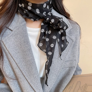 Detailed view of a black polka dot silk scarf tied in a bow over a grey wool blazer