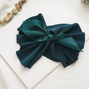 Macro detail of large dark green fabric bow hair clip on a minimalist aesthetic background