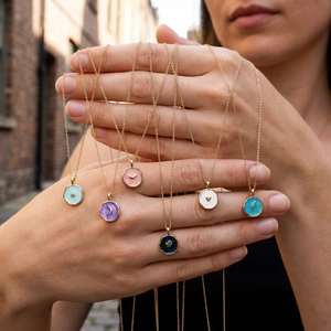 Colorful enamel star and heart pendants on gold necklaces held in a hand outdoors