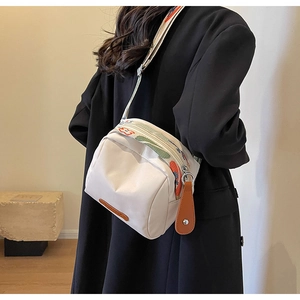Dettaglio borsa a tracolla in tela bianca con cinturino colorato indossata su blazer nero
