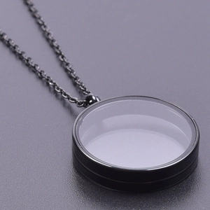 Detailed view of a black round glass locket pendant with a thin metal chain necklace