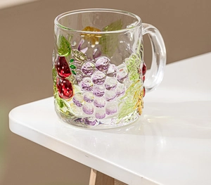 Detail of transparent glass mug with hand-painted strawberry and grape 3D relief patterns