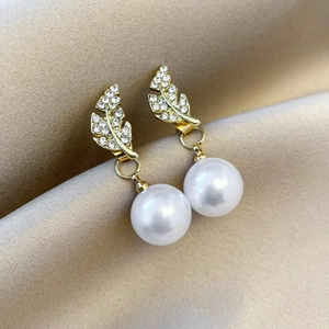 Detail of elegant gold leaf earrings with rhinestones and hanging white pearls