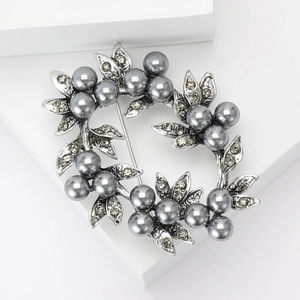 Elegant silver floral wreath brooch with dark grey pearls and rhinestones on white stand