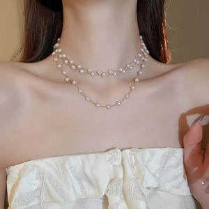 Détail d'un collier double rang doré avec perles blanches rondes sur le mannequin