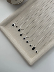 Macro view of S925 sterling silver necklaces with black onyx pendants on beige velvet tray