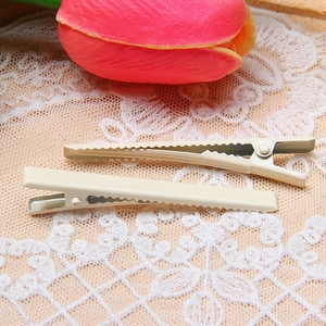 Close-up of two cream-colored 6cm slim duckbill metal hair clips on white floral lace fabric