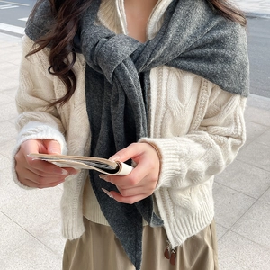 Detail eines dunkelgrauen Strickschals kombiniert mit einer cremefarbenen Strickjacke