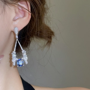 Close-up of dangling silver earrings with blue square crystal and zircon inlays on model