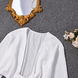 Mise à plat d'un cardigan blanc texturé à manches longues sur un tapis gris foncé