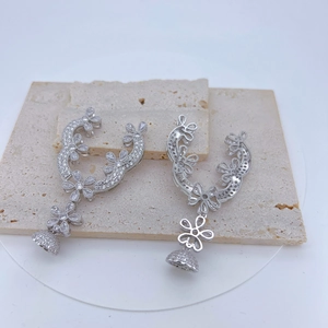 Macro detail of silver floral drop earrings with white zircons on a beige stone base