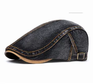 Detail of black denim flat cap featuring orange contrast stitching and brown leather brim