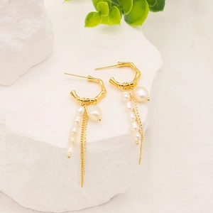 Close-up of gold C-shape earrings with irregular natural pearls and long metal tassels