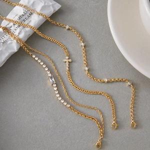 Détail de bracelets superposés en zircon doré avec pendentif croix et fermoir mousqueton chic